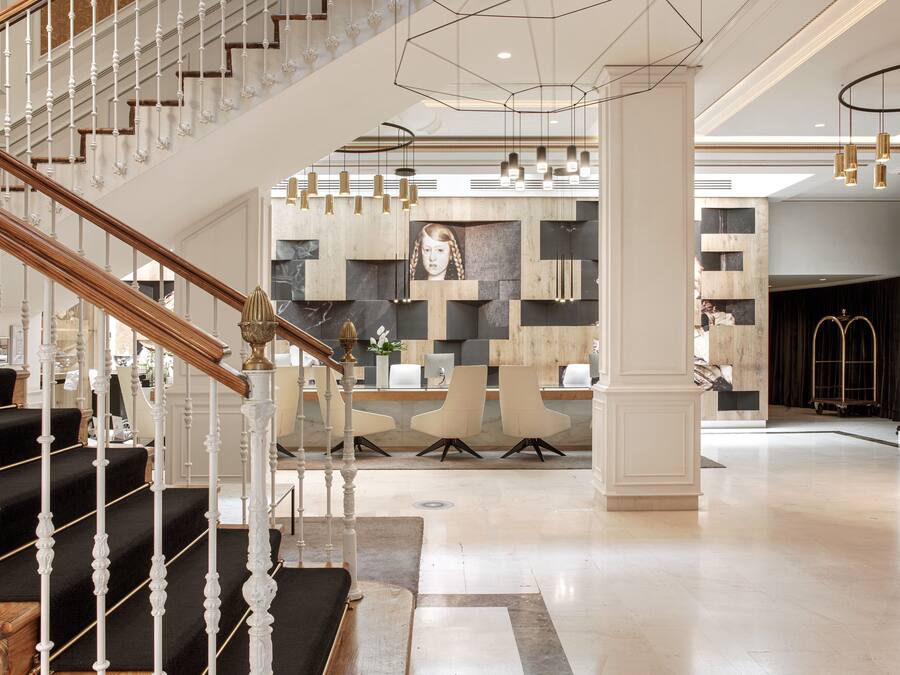 Een ruime lobby met een statige trap, een moderne zithoek en een grote muur met een geometrisch patroon.