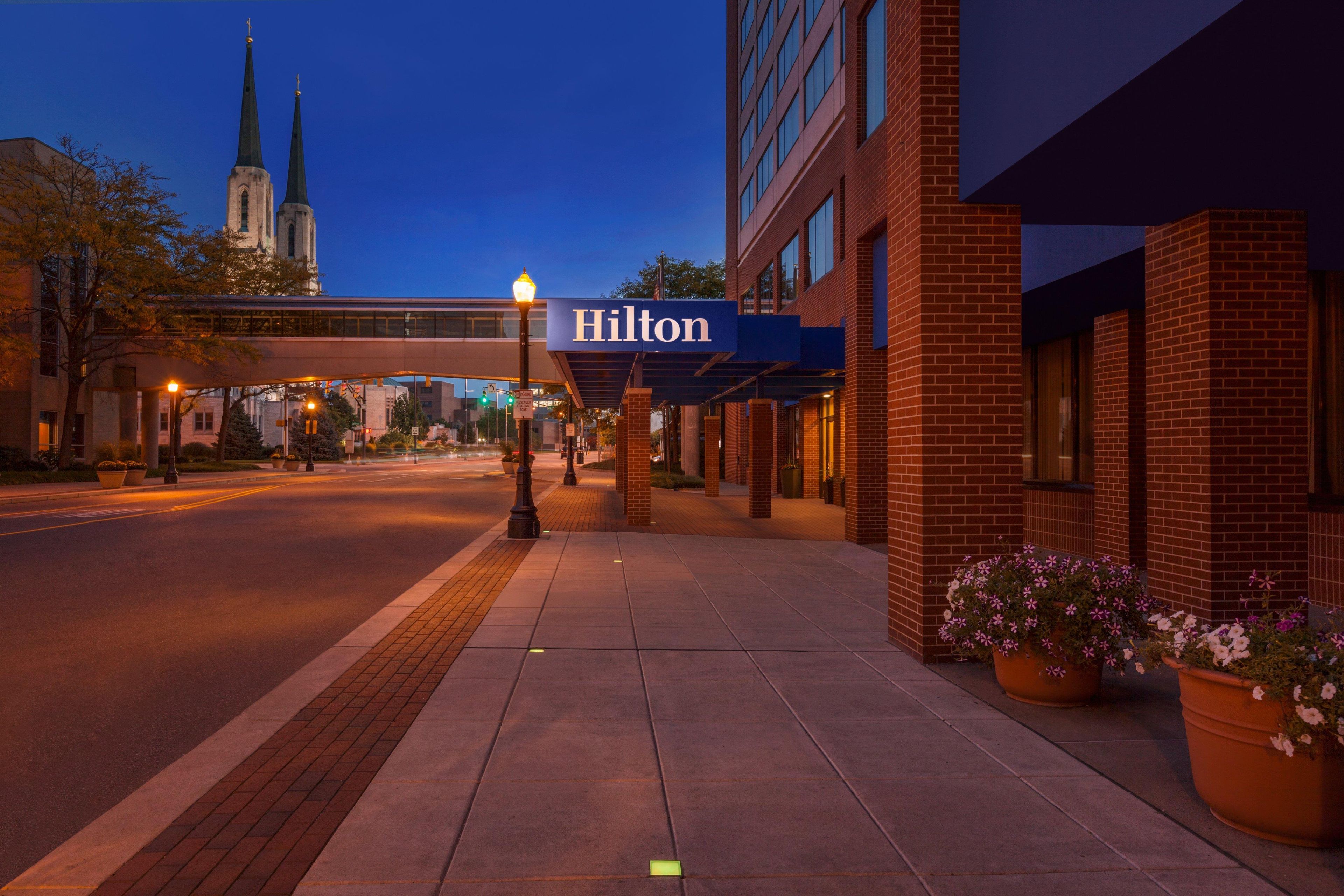 A hotel entrance with a sign, a street, and a church spire in the background.
