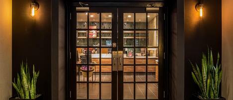 A Starbucks entrance with a dark facade, double doors, and two potted plants on either side.
