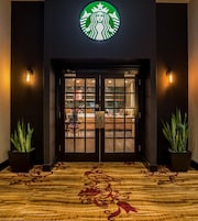 Entrada de Starbucks con fachada oscura, puertas dobles y dos plantas en macetas a cada lado.
