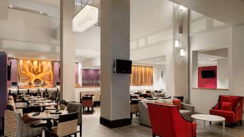 A spacious hotel lobby with multiple seating areas, a bar, and a television screen.