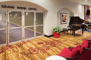 Un vestíbulo de hotel con un piano de cola, sillas rojas, una planta en maceta y una alfombra con estampado rojo y dorado.