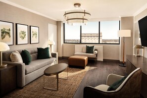 Una habitación de hotel moderna con sofá, sillón, reposapiés y un ventanal con vistas a la ciudad.