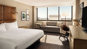 A hotel room with a large bed, a sofa, a desk, and a television. There are framed pictures on the wall and a window with a view of a building. - Hilton Fort Wayne at the Grand Wayne Convention Center (Fort Wayne)