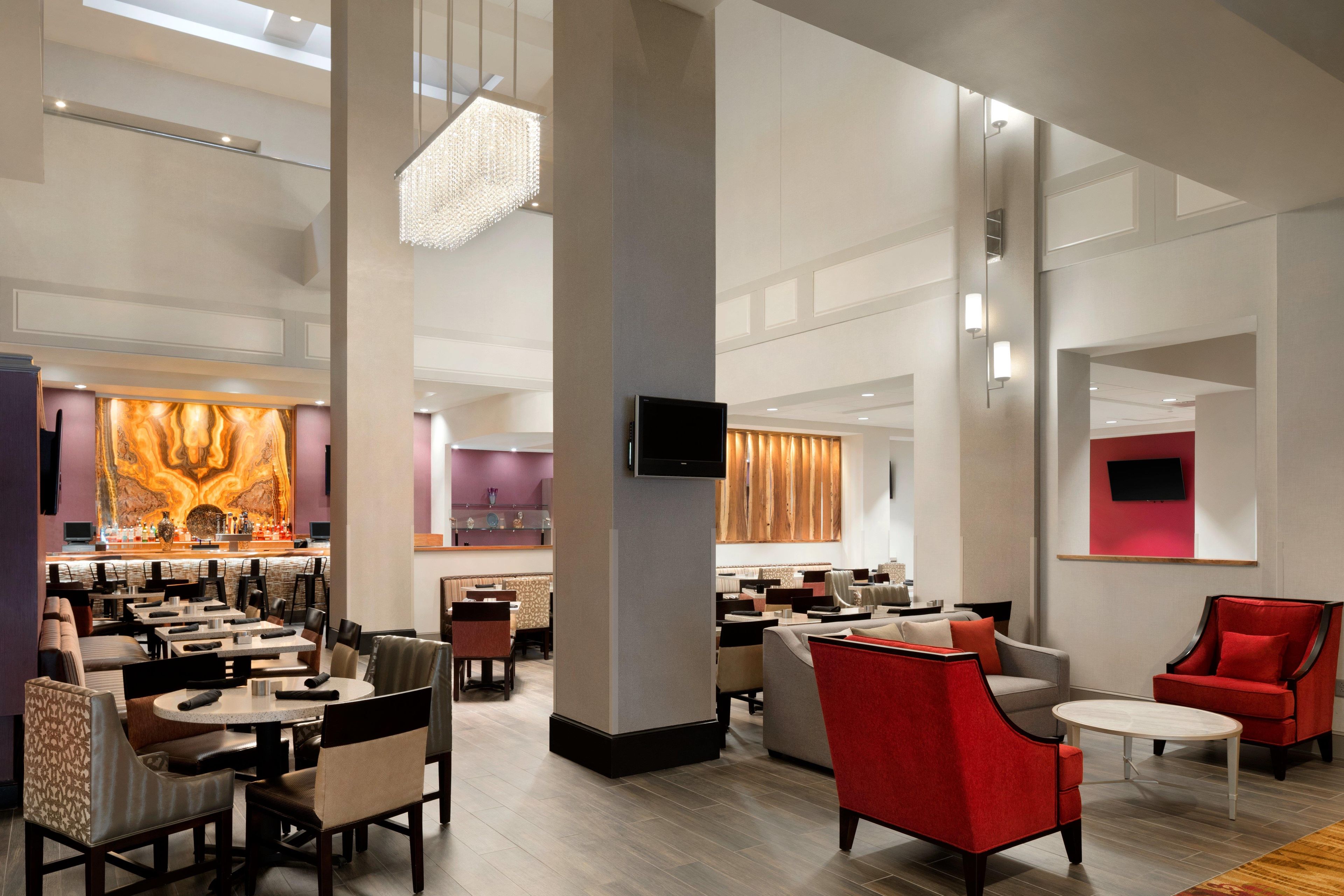 A spacious hotel lobby with multiple seating areas, a bar, and a television screen.
