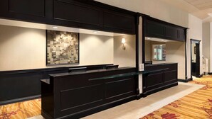A reception area with a black reception desk, a patterned wall, and a carpeted floor. - Hilton Fort Wayne at the Grand Wayne Convention Center (Fort Wayne)