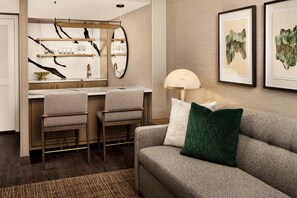A modern hotel room with a kitchenette, a sofa, and a dining area.