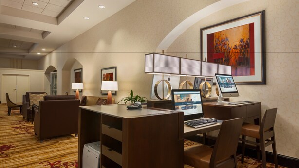 A hotel room with a desk, two computers, a printer, a lamp, and a large painting on the wall. - Hilton Fort Wayne at the Grand Wayne Convention Center (Fort Wayne)