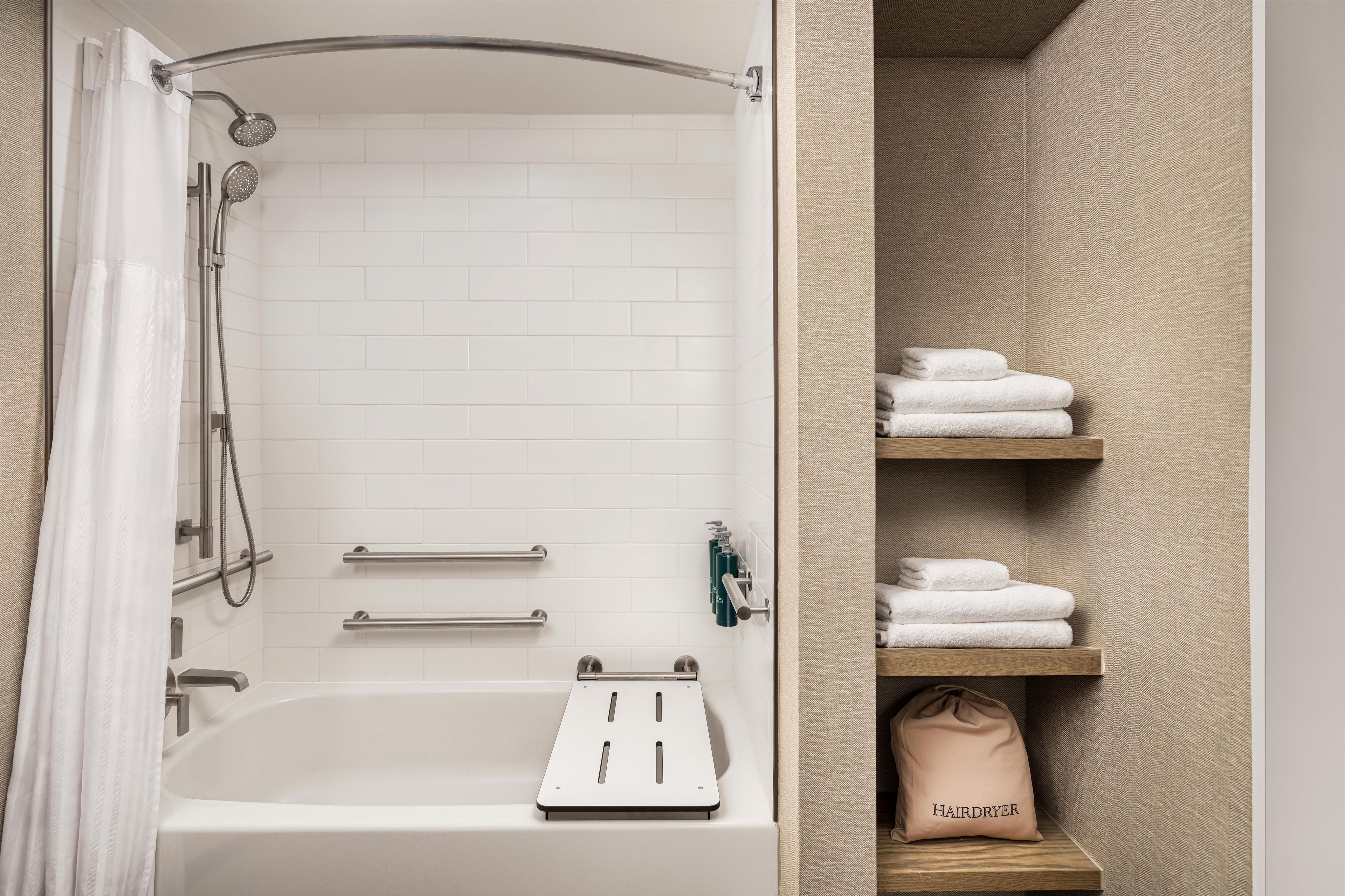 A bathroom with a bathtub, shower, towel rack, and a hairdryer on a shelf.