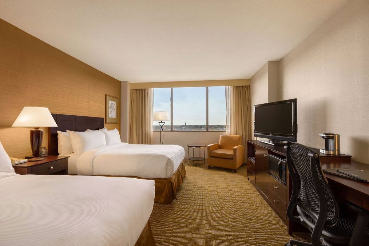 A hotel room with two beds, a television, a desk, and a chair.