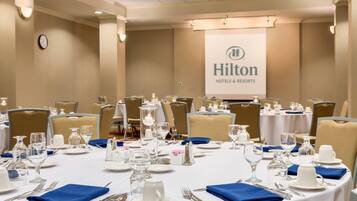 A conference room with round tables set for a meeting, equipped with nameplates, water glasses, and a projector screen displaying the Hilton Hotels & Resorts logo.