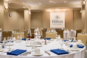 A conference room with round tables set for a meeting, equipped with nameplates, water glasses, and a projector screen displaying the Hilton Hotels & Resorts logo. - Hilton Fort Wayne at the Grand Wayne Convention Center (Fort Wayne)