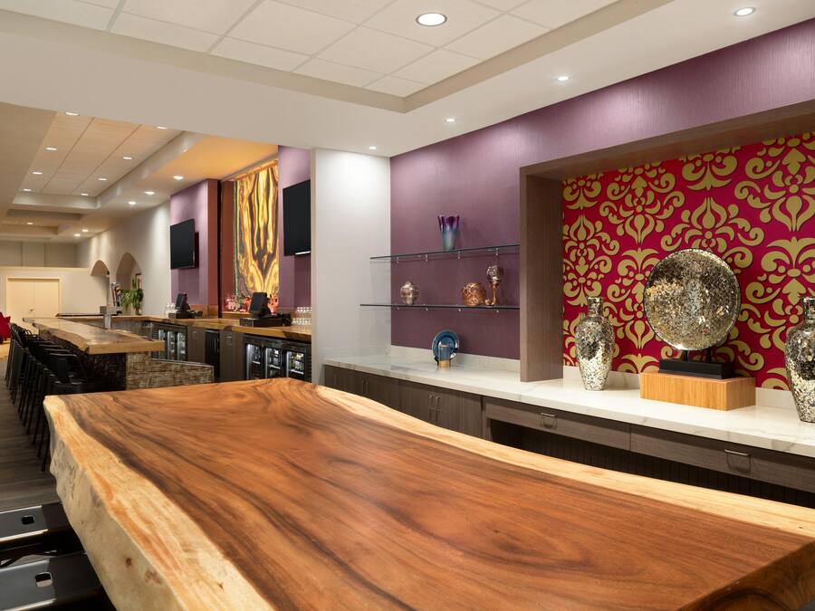 Een moderne bar met een houten toonbank, planken met decoratieve items en een patroonbehang in de achtergrond.