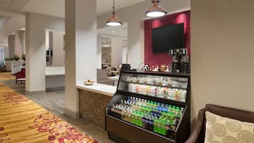Un hall de hotel con dispensador de bebidas, zona de estar y un mostrador de recepción.