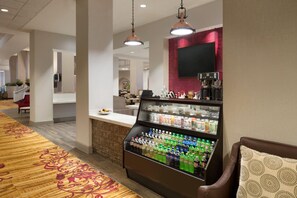 Un hall de hotel con dispensador de bebidas, zona de estar y un mostrador de recepción.