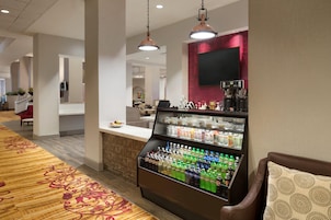 Un hall de hotel con dispensador de bebidas, zona de estar y un mostrador de recepción.