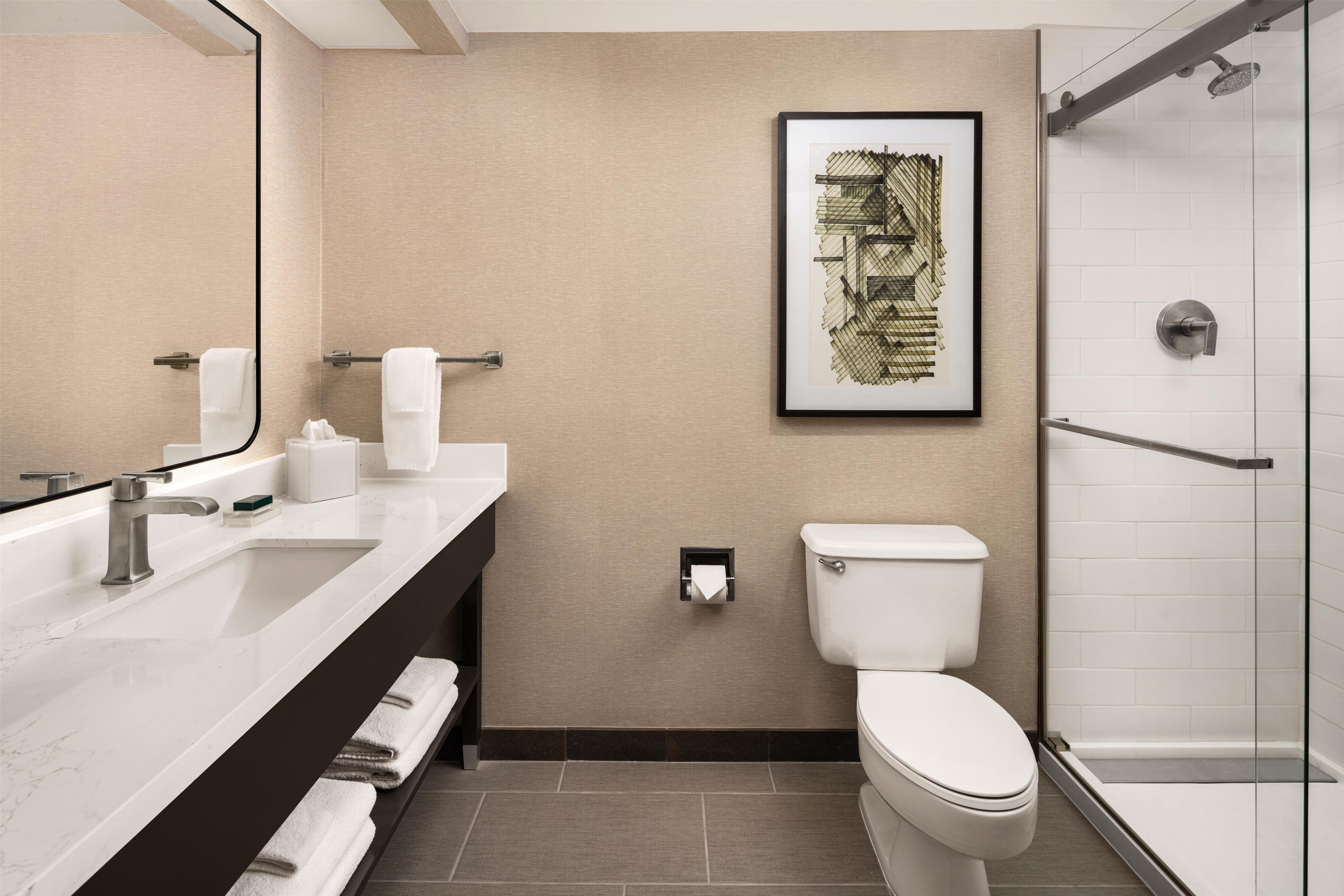 Un baño moderno con lavamanos, espejo, inodoro y ducha blancos.