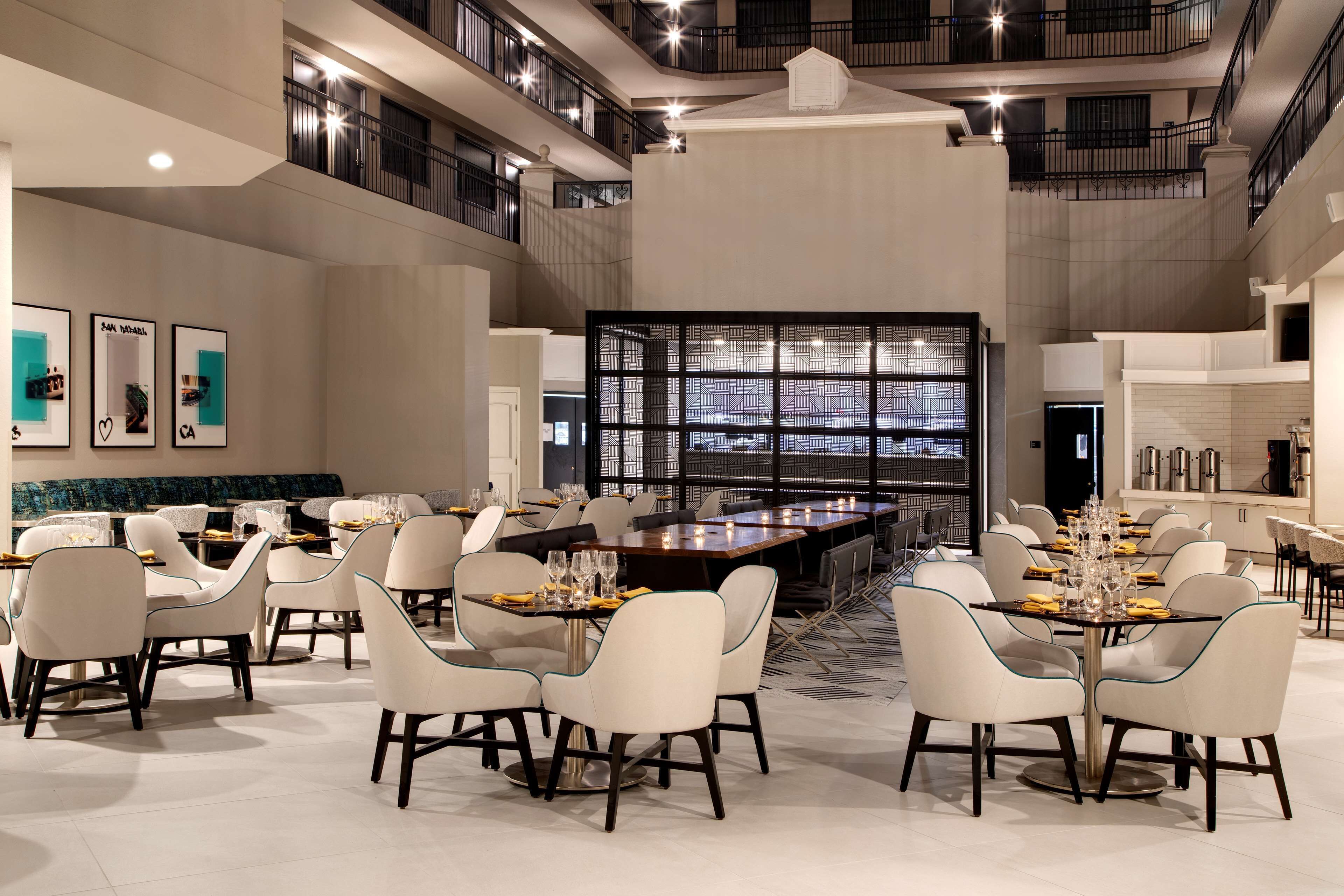 Un comedor espacioso con varias mesas y sillas, un gran ventanal y un diseño de interiores moderno.