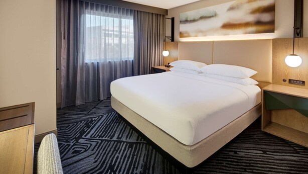 A hotel room with a large bed, a desk, a chair, a nightstand, a lamp, and a painting on the wall. - Embassy Suites by Hilton San Rafael at Marin Center (San Rafael)