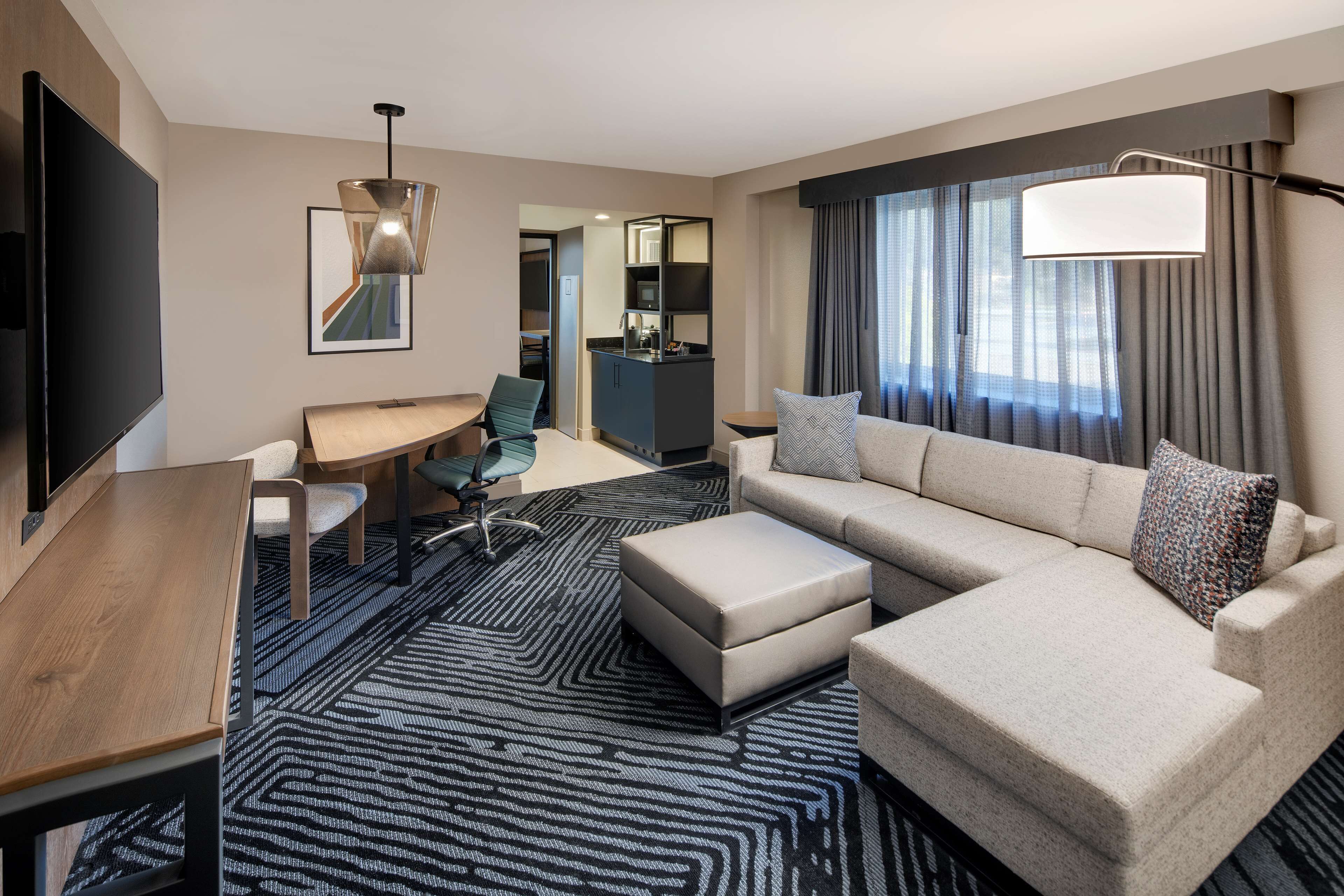 Una habitación de hotel moderna con una gran televisión de pantalla plana, un sofá, una mesa de comedor y una kitchenette.
