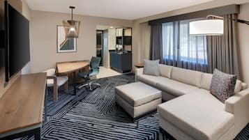 Una habitación de hotel moderna con una gran televisión de pantalla plana, un sofá, una mesa de comedor y una kitchenette.