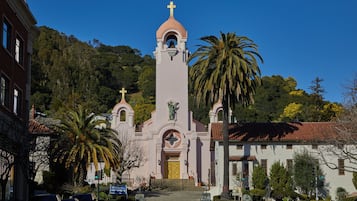 A church with a bell tower and a cross, surrounded by palm trees and a hilly landscape.