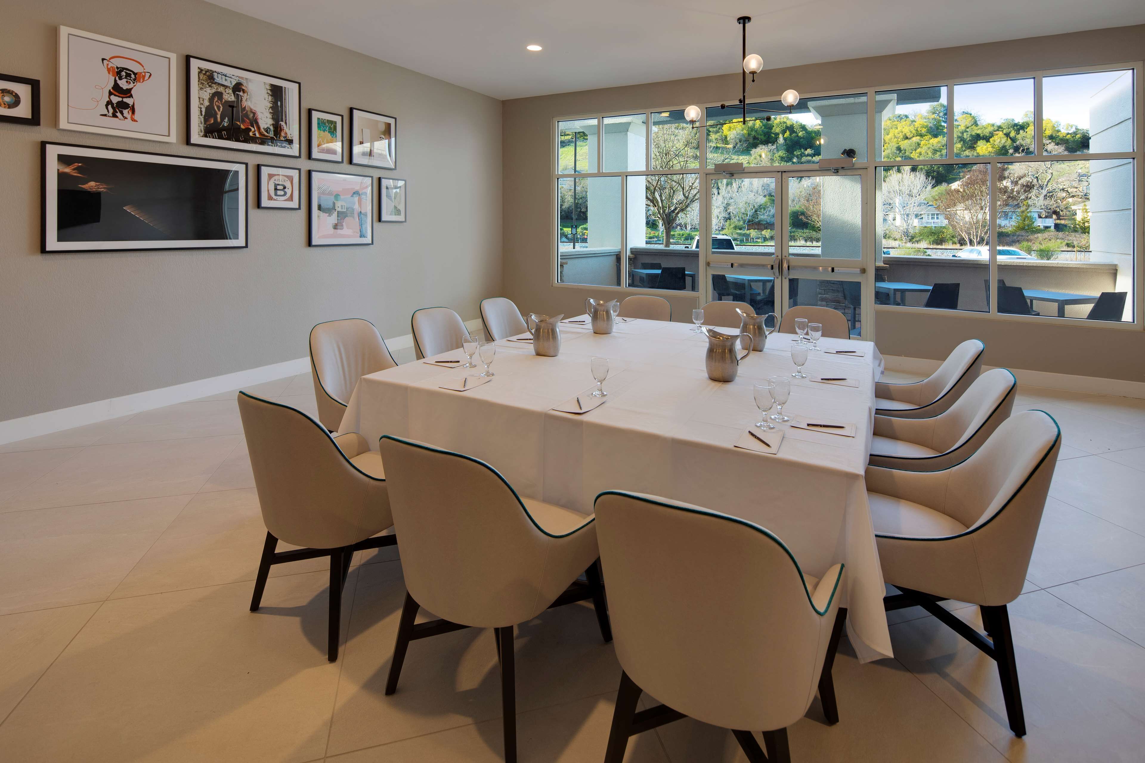 Un comedor con una mesa grande dispuesta para seis personas, rodeada por seis sillas, con obras de arte en las paredes y vistas al exterior a través de amplias ventanas.
