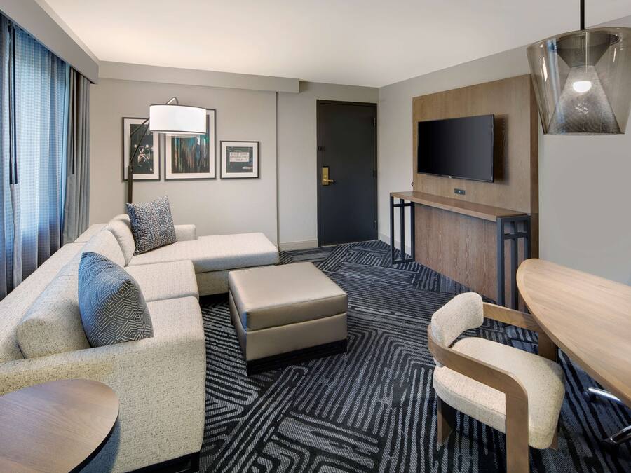 A modern hotel room with a sofa, ottoman, and a dining table.