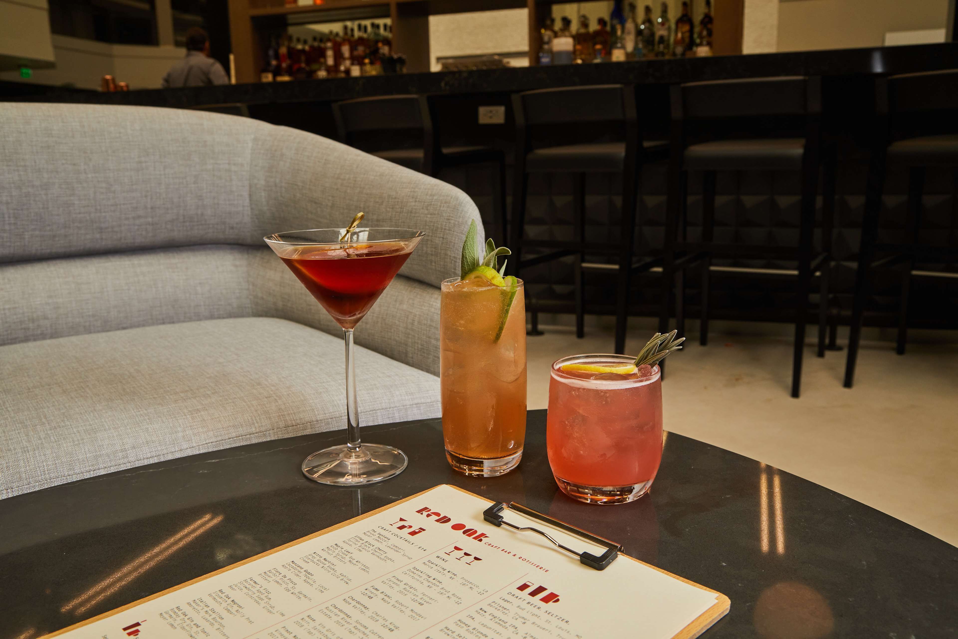 A bar area with three drinks on a table, a menu, and a bar counter in the background.
