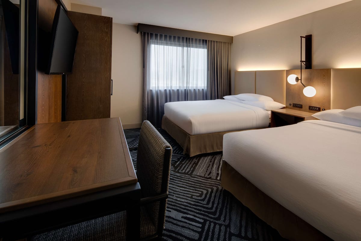 A hotel room with two beds, a desk, a chair, and a television.
