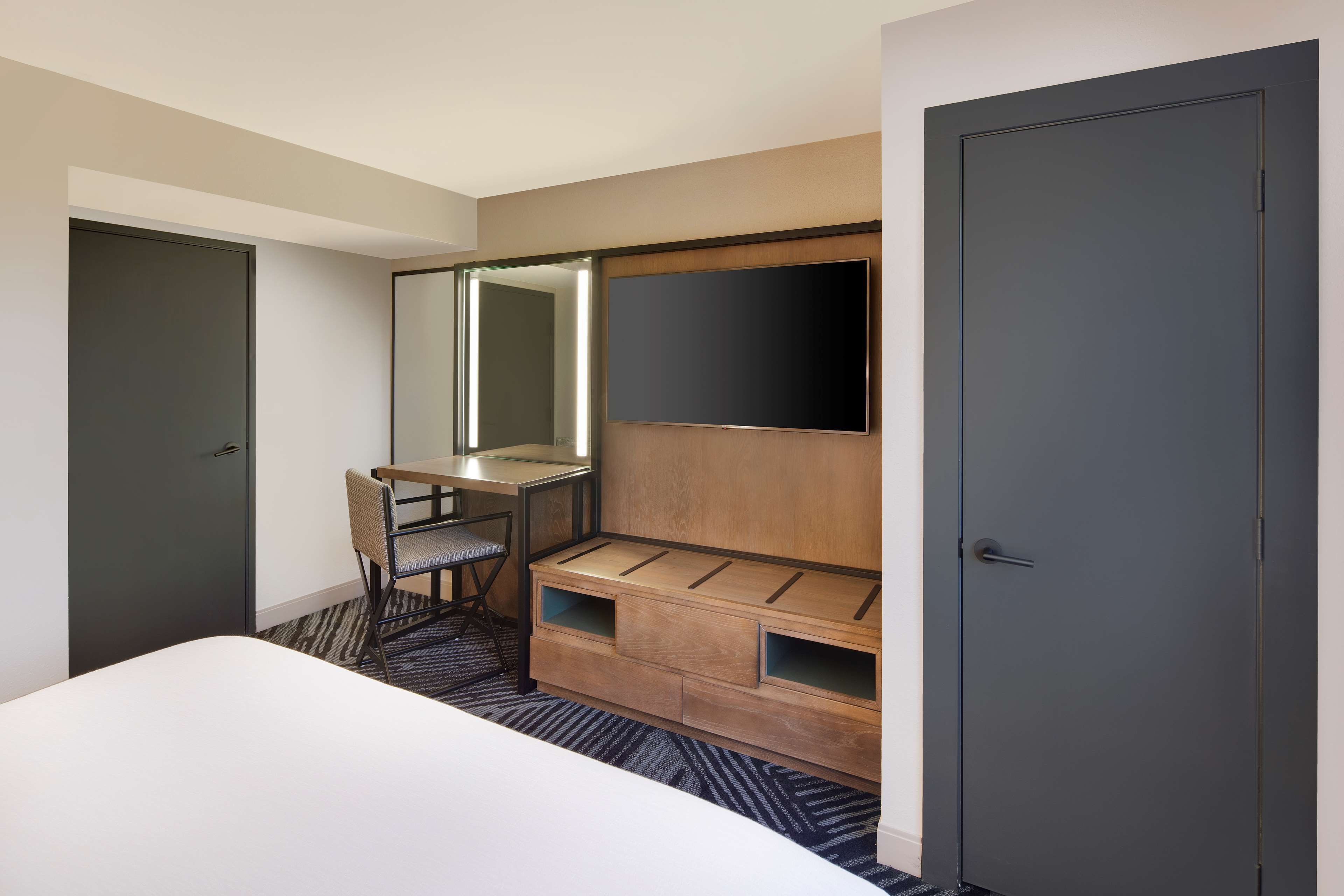 Ein Hotelzimmer mit Bett, Schreibtisch mit Stuhl, einem großen Spiegel und einem Kleiderschrank.