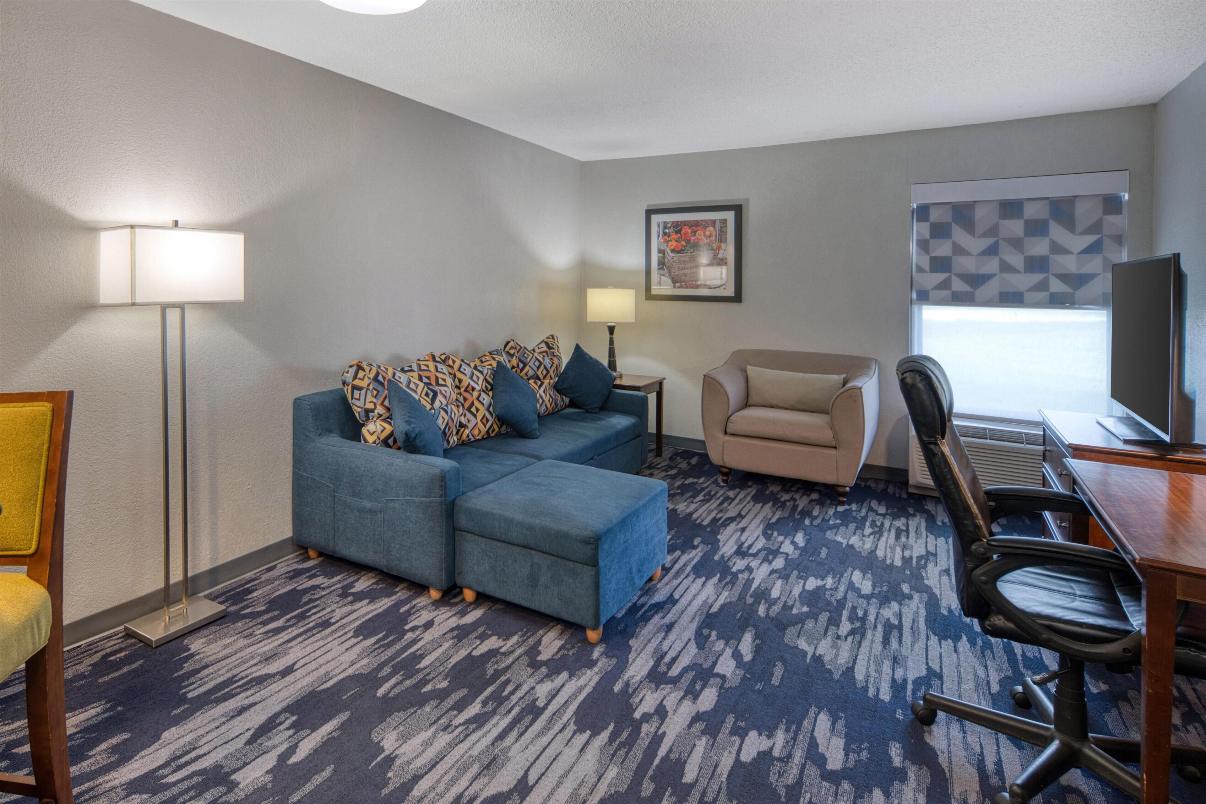 A hotel room with a sectional sofa, a chair, a desk, and a lamp.