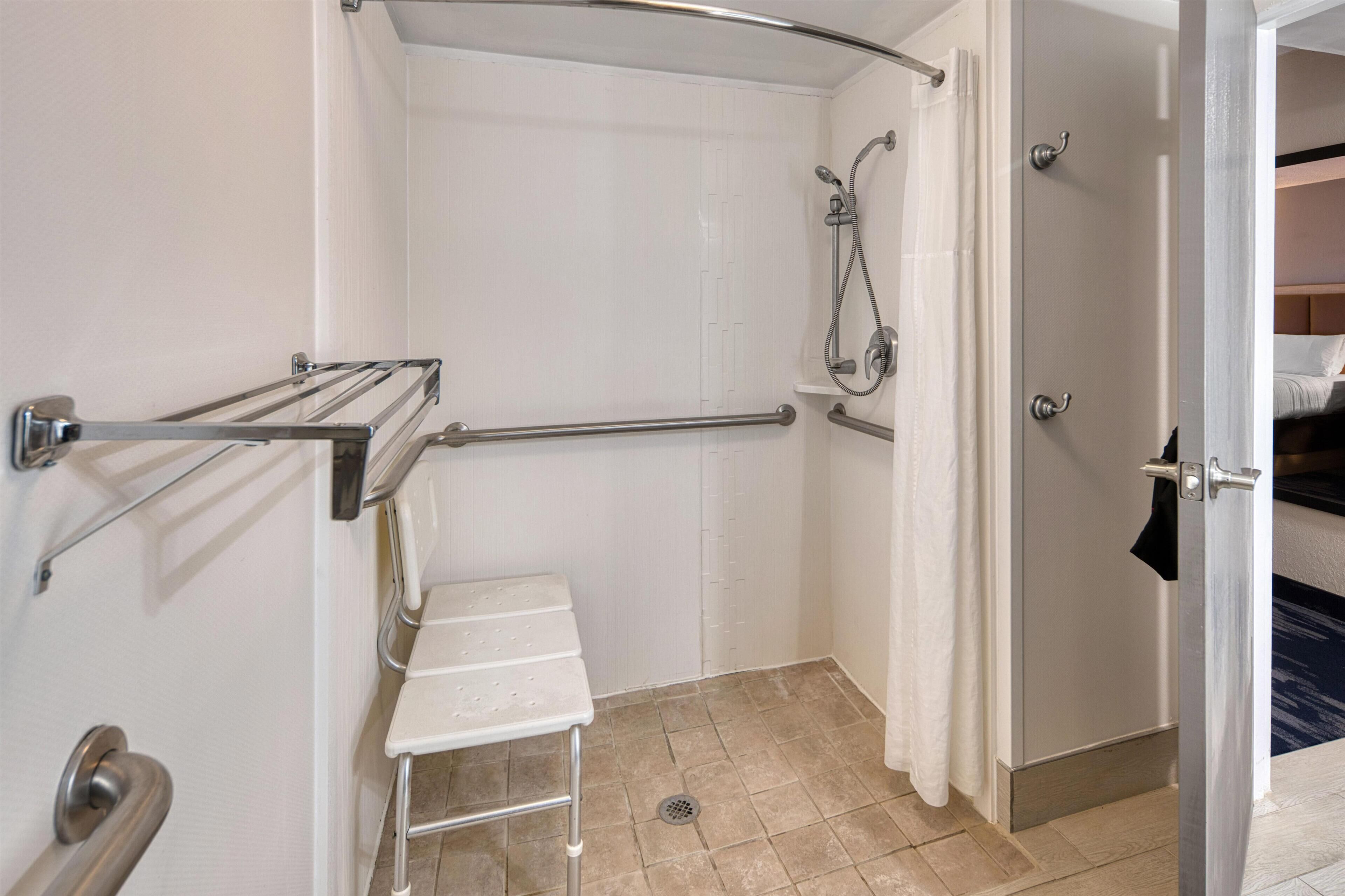 A bathroom with a shower, grab bars, a sink, and a door leading to a bedroom.