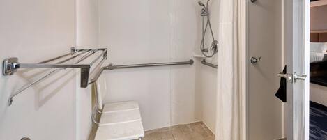 A bathroom with a shower, grab bars, a sink, and a door leading to a bedroom.
