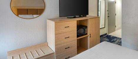 Habitación de hotel con cama, televisión, microondas, cómoda de madera, espejo y puerta que da a otra habitación.