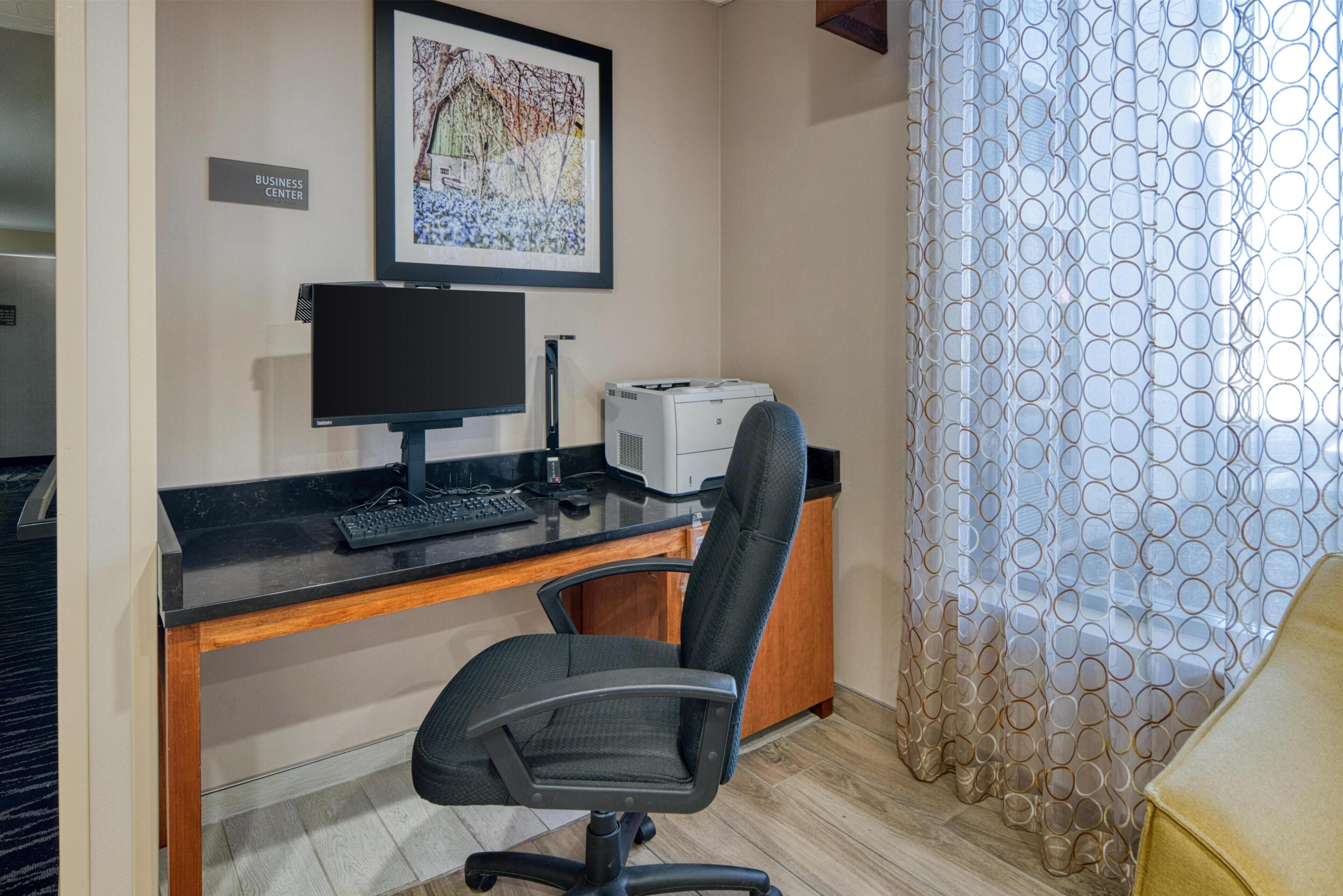 A business center with a desk, computer, printer, and a chair.