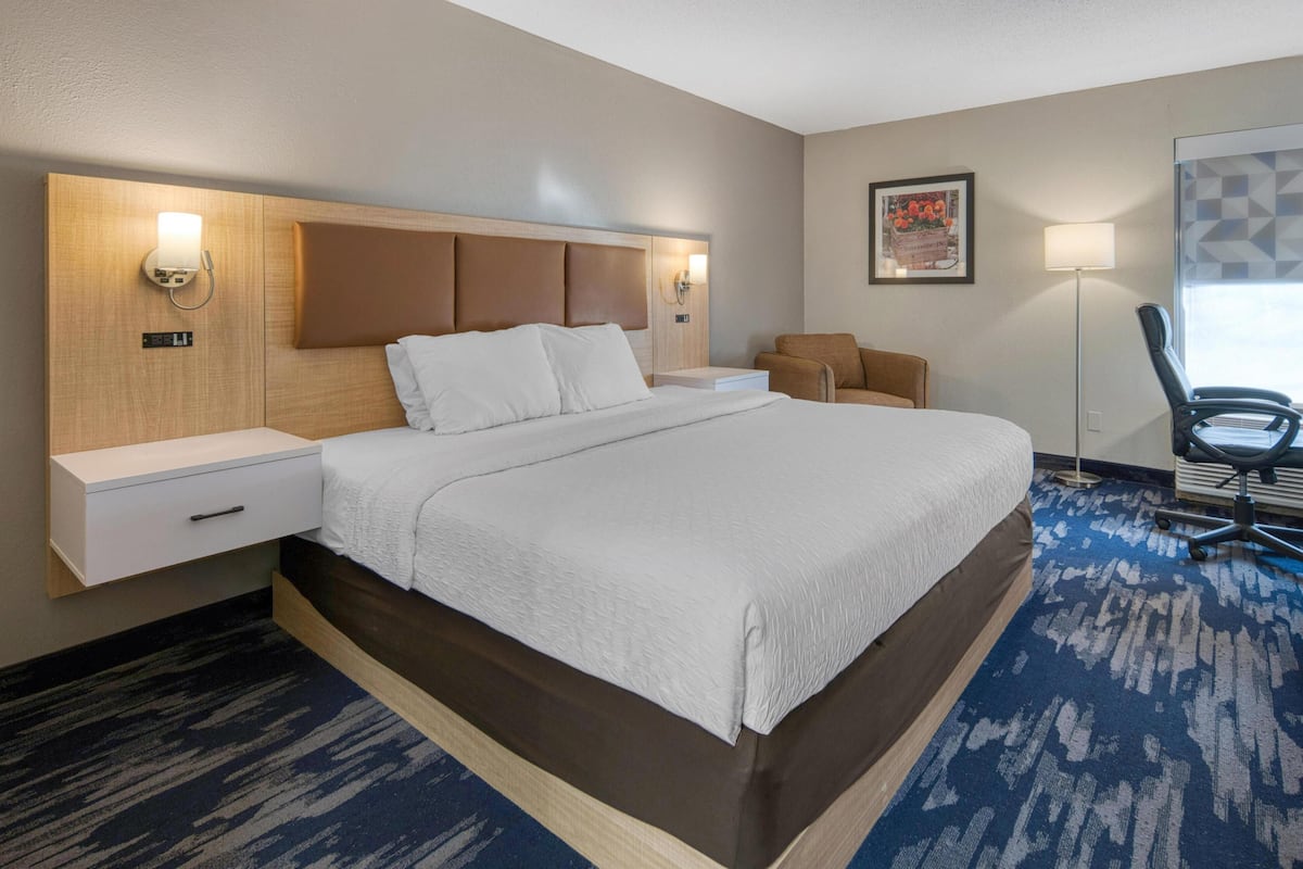Ein Hotelzimmer mit einem großen Bett, Nachttischen, einem Schreibtisch, einem Stuhl und einer Lampe.