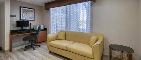 Une pièce avec un canapé jaune, un bureau avec un ordinateur, une chaise et une petite table.