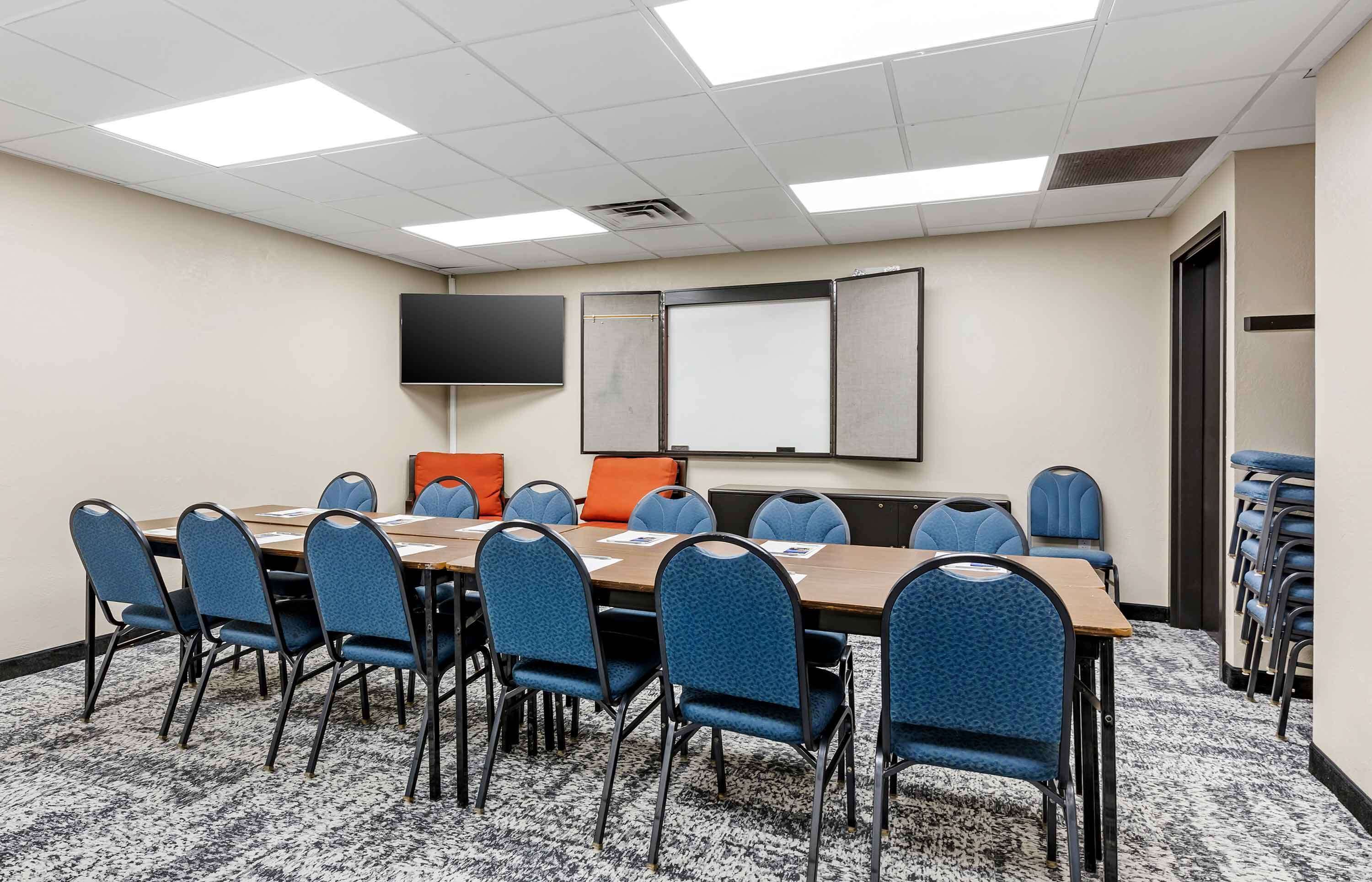 Un salón de conferencias con una larga mesa, sillas azules, una pantalla de proyector y una pizarra.