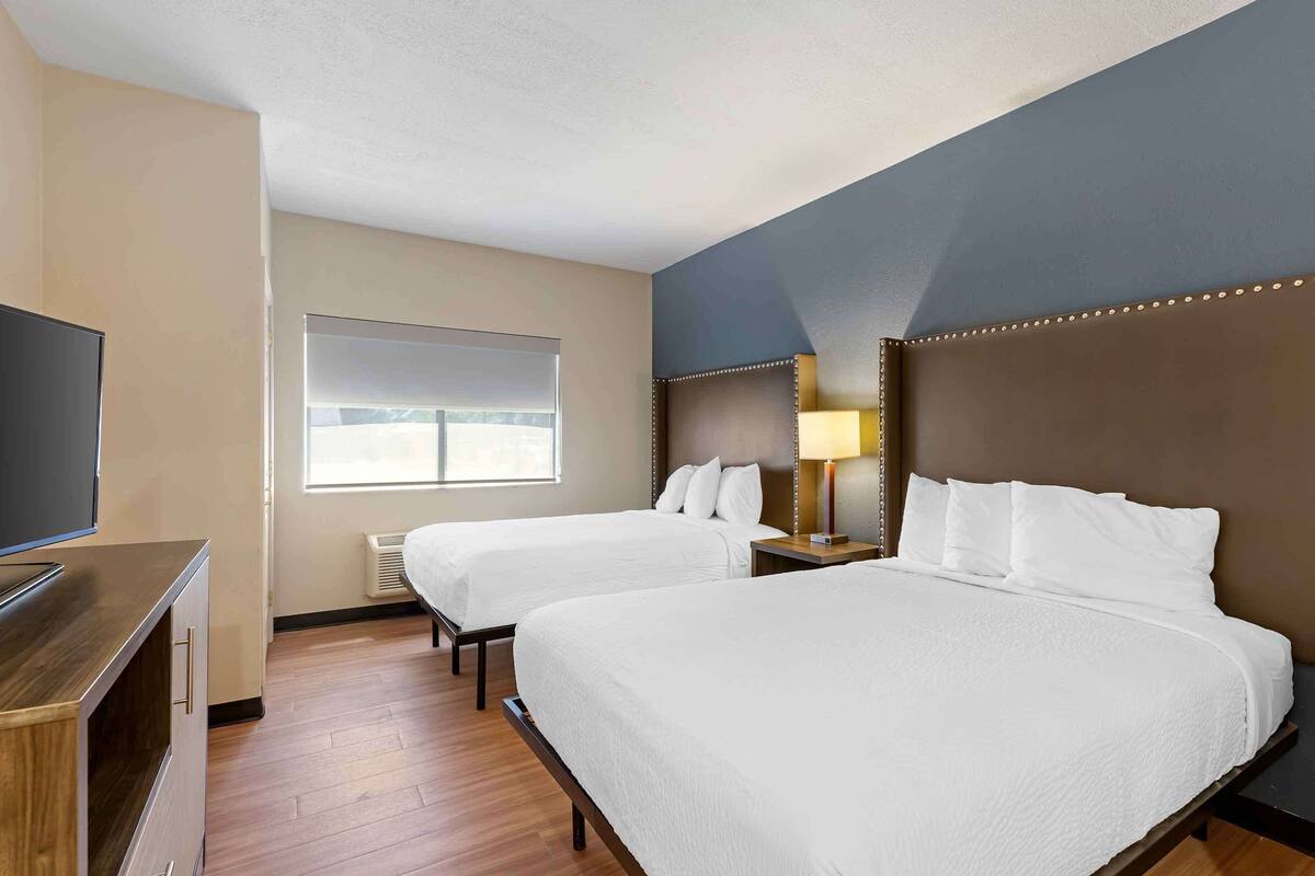 A hotel room with two beds, a TV, a window, and a lamp.