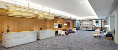 A spacious lobby with a marble reception desk, comfortable seating, and a large glass wall offering a view of the kitchen area.
