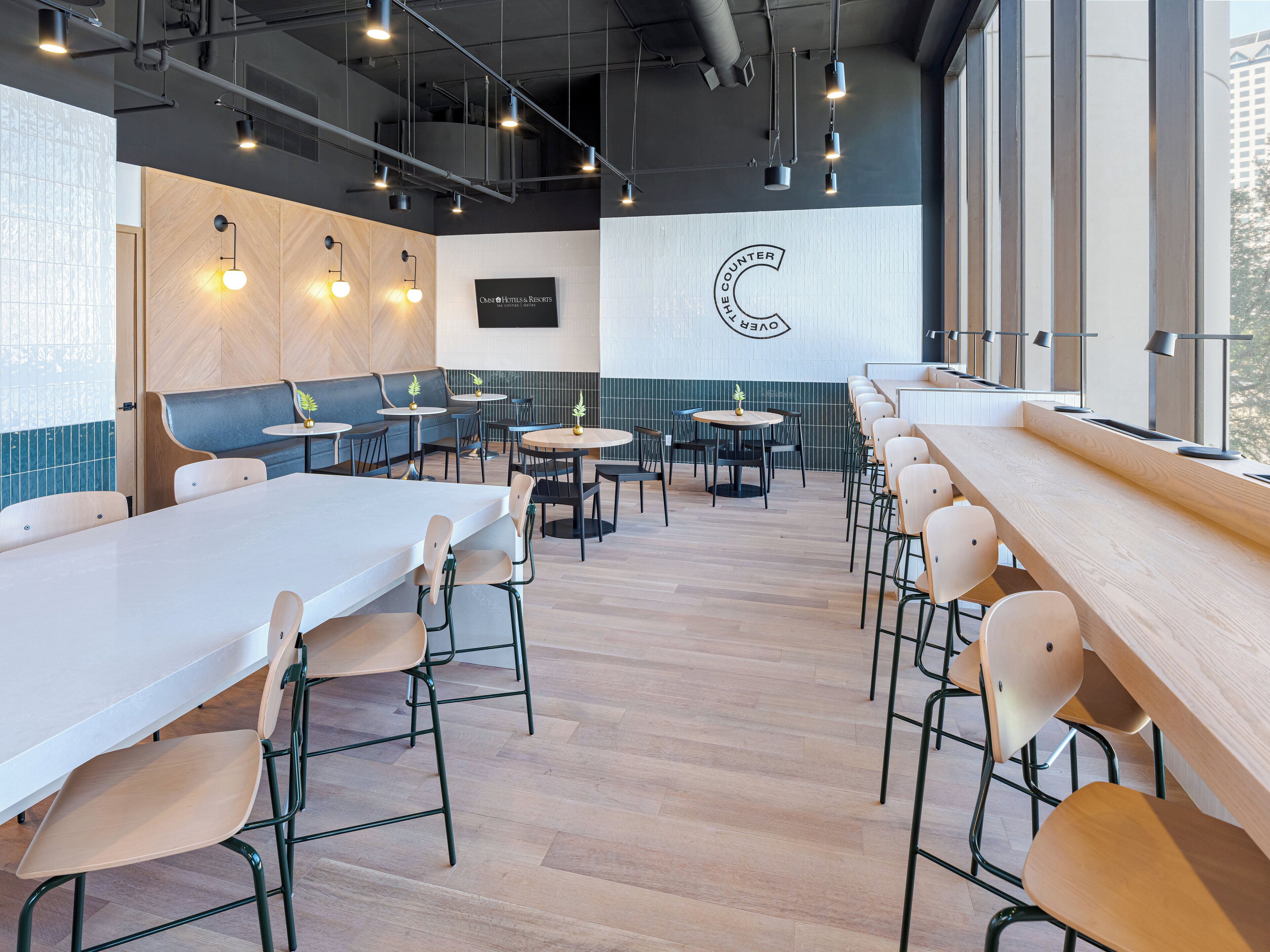 Un intérieur de restaurant moderne avec des tables hautes, des banquettes et un grand logo fixé au mur.