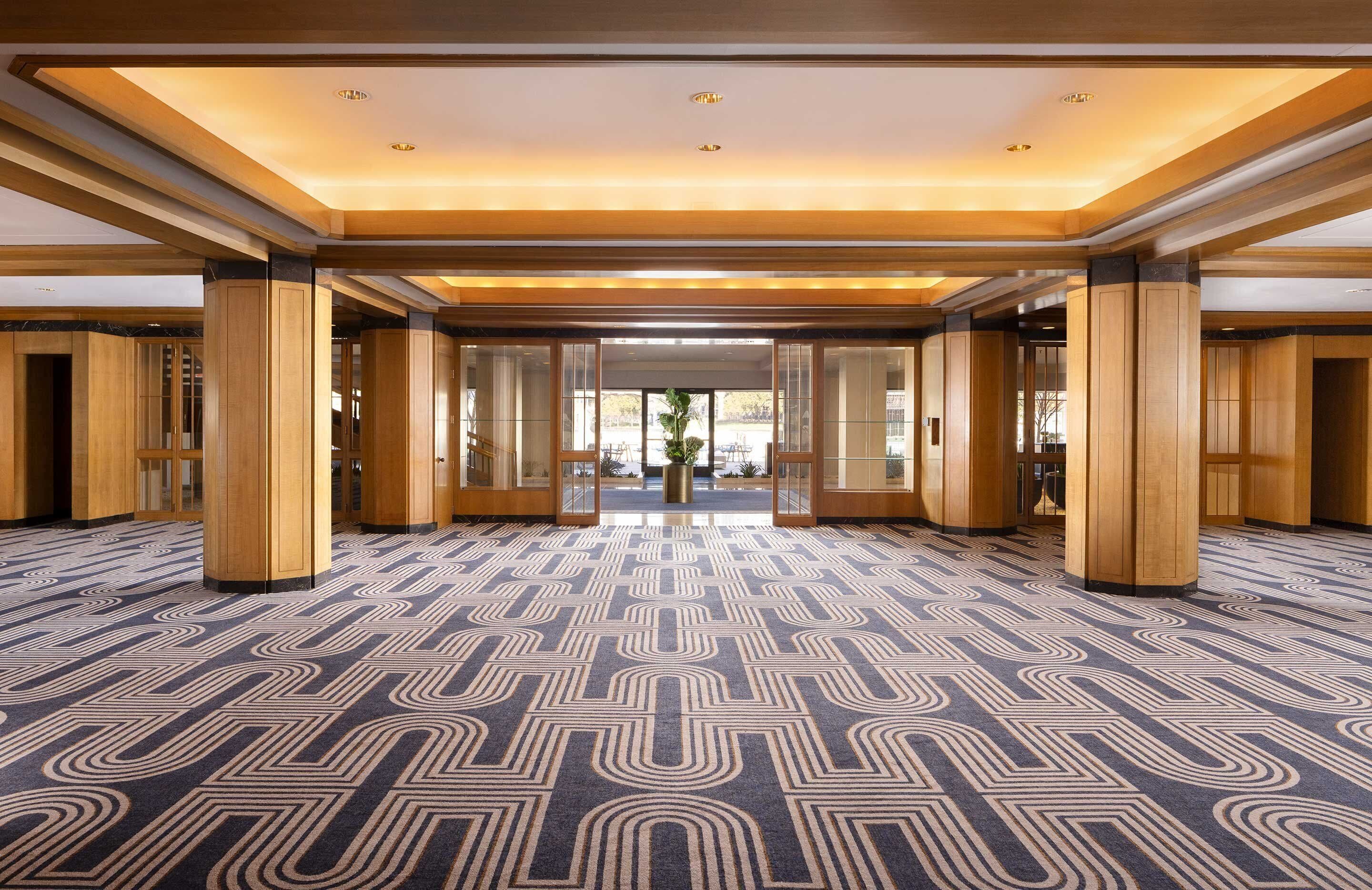 A spacious lobby with a geometric patterned carpet, wooden columns, and a modern ceiling design.