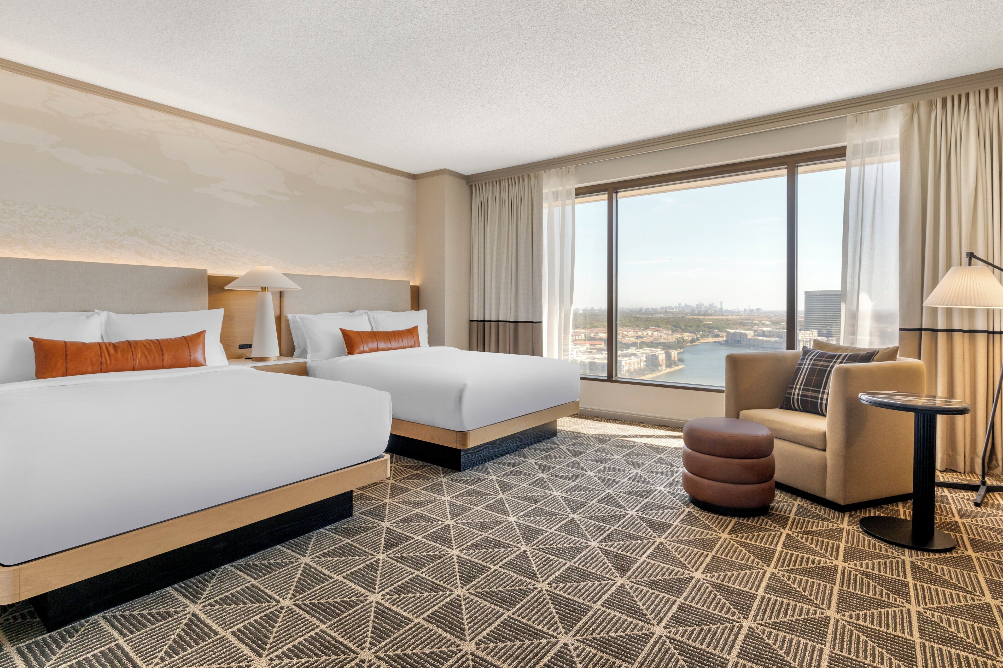 A hotel room with two beds, a sofa, a small table, and a large window offering a city view.