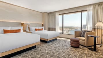 A hotel room with two beds, a sofa, a small table, and a large window offering a city view.