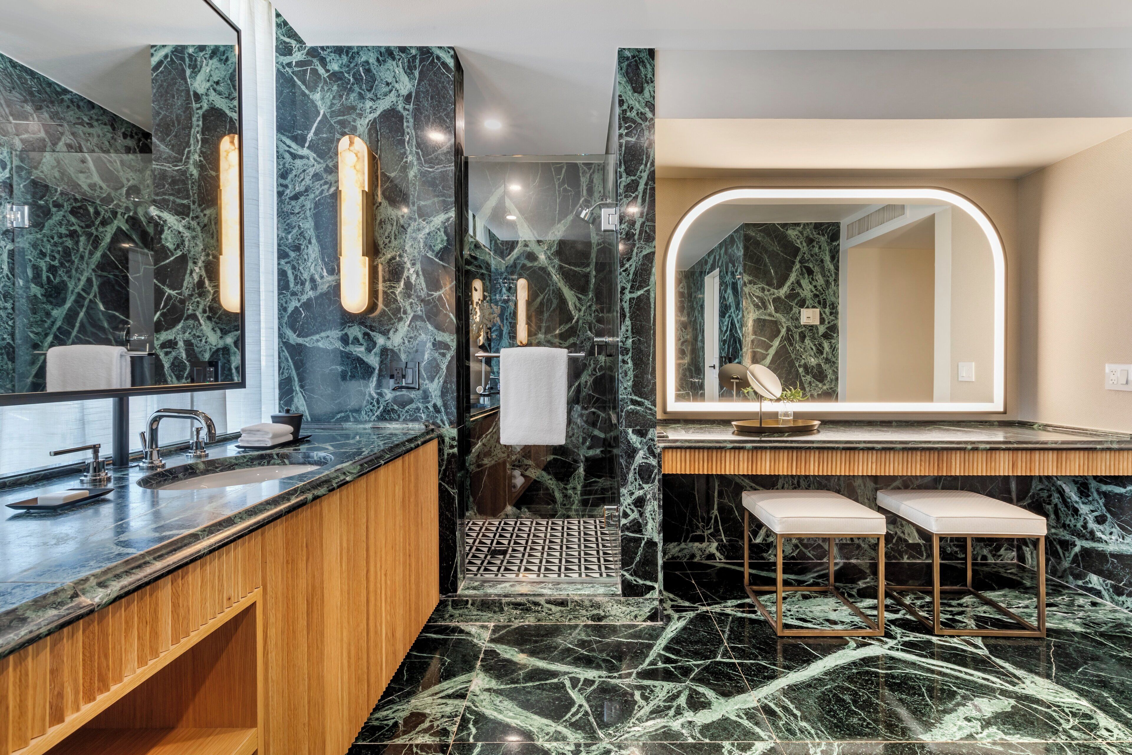 A modern bathroom with marble walls, a large mirror, and a wooden vanity.