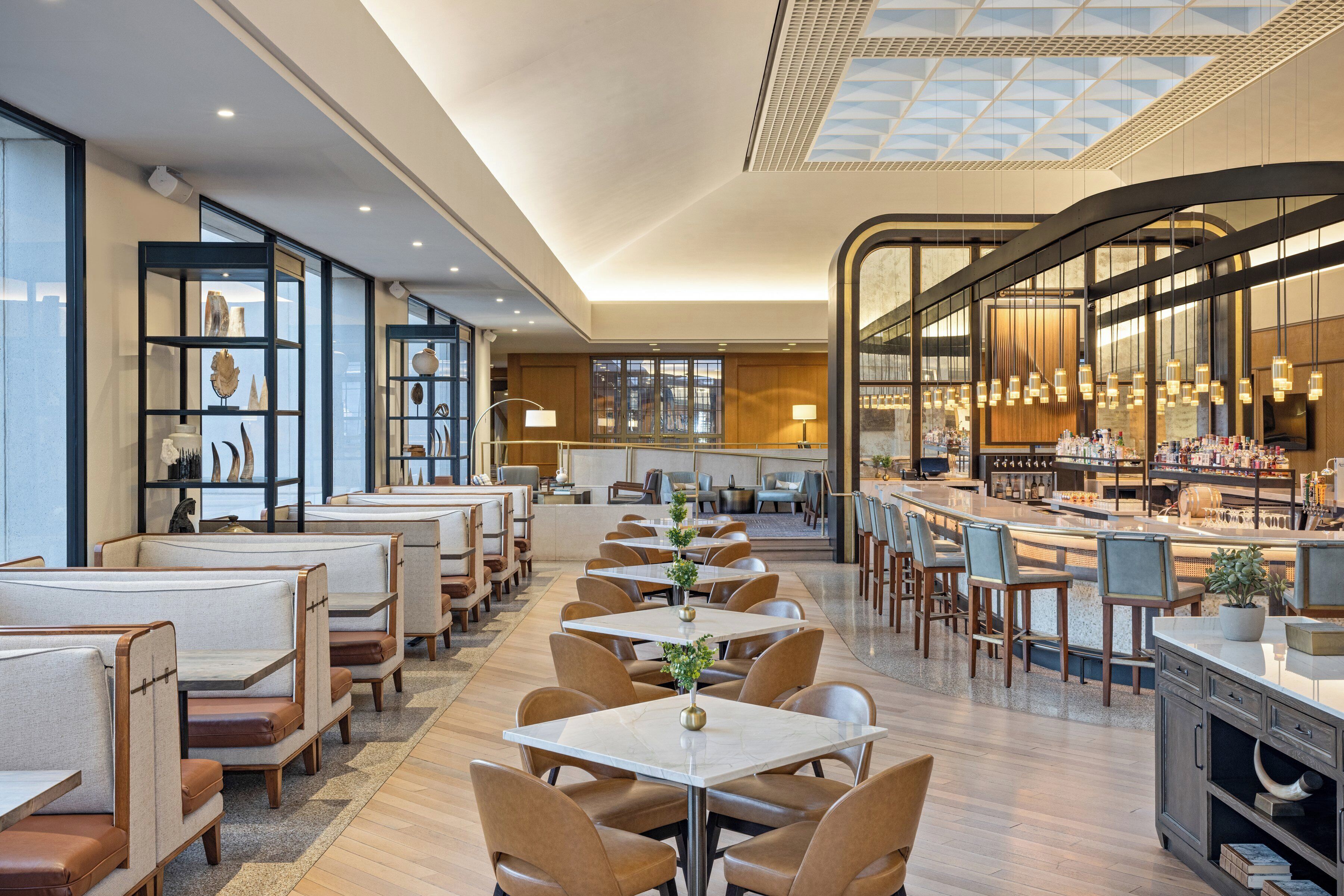 A modern restaurant with high ceilings, glass partitions, and a variety of seating options including booths and tables.