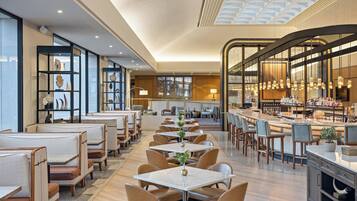 A modern restaurant with high ceilings, glass partitions, and a variety of seating options including booths and tables.
