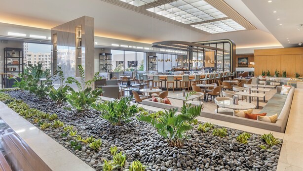A spacious indoor area with multiple seating arrangements, a central water feature, and a view of the cityscape through large windows. - Omni Las Colinas Hotel (Irving)