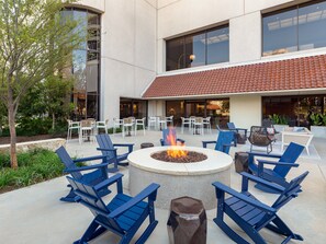 An outdoor seating area with blue Adirondack chairs, a fire pit, and a patio with tables and chairs. - Omni Las Colinas Hotel (Irving)